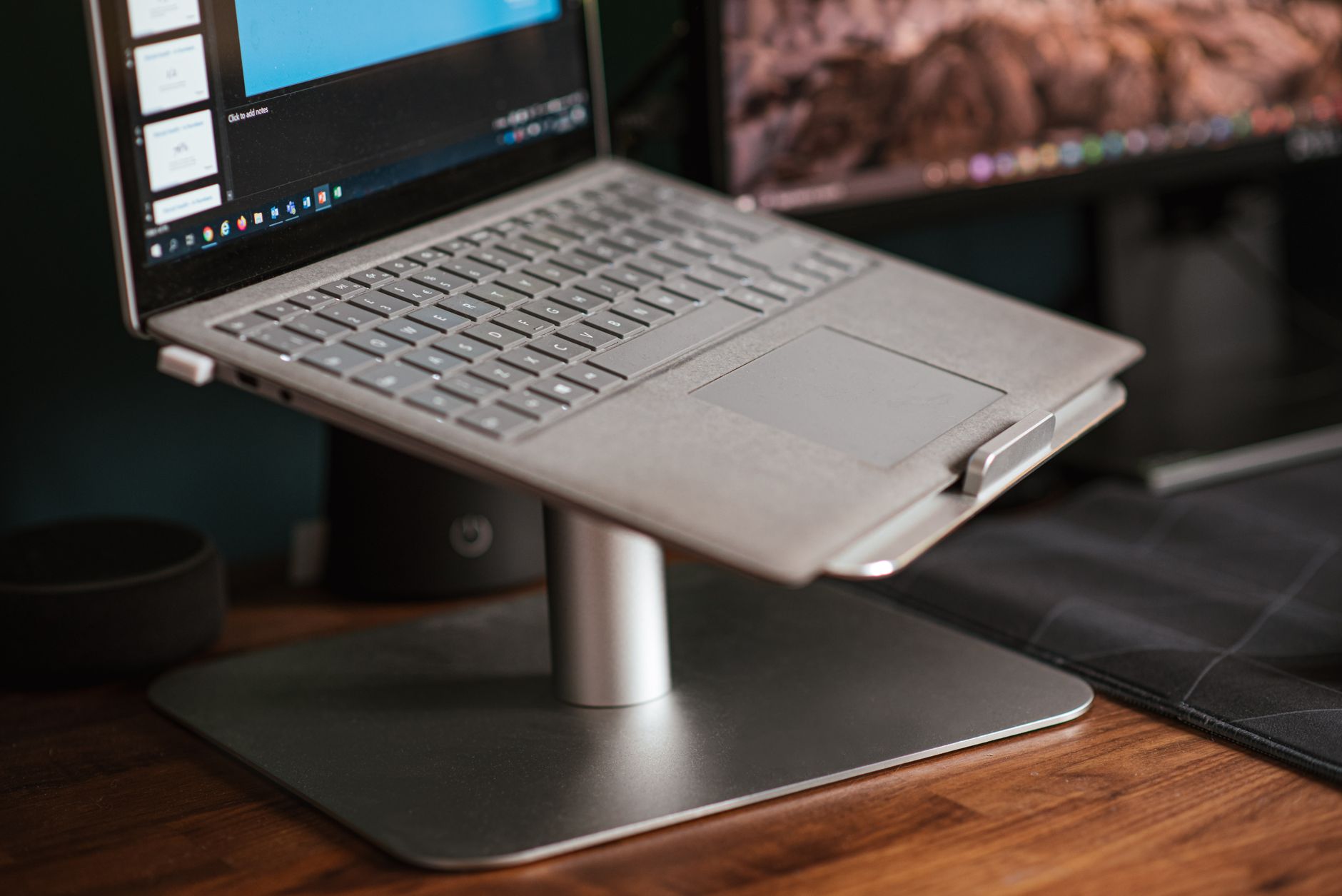 A compact foldable laptop stand holding a silver laptop on an office desk