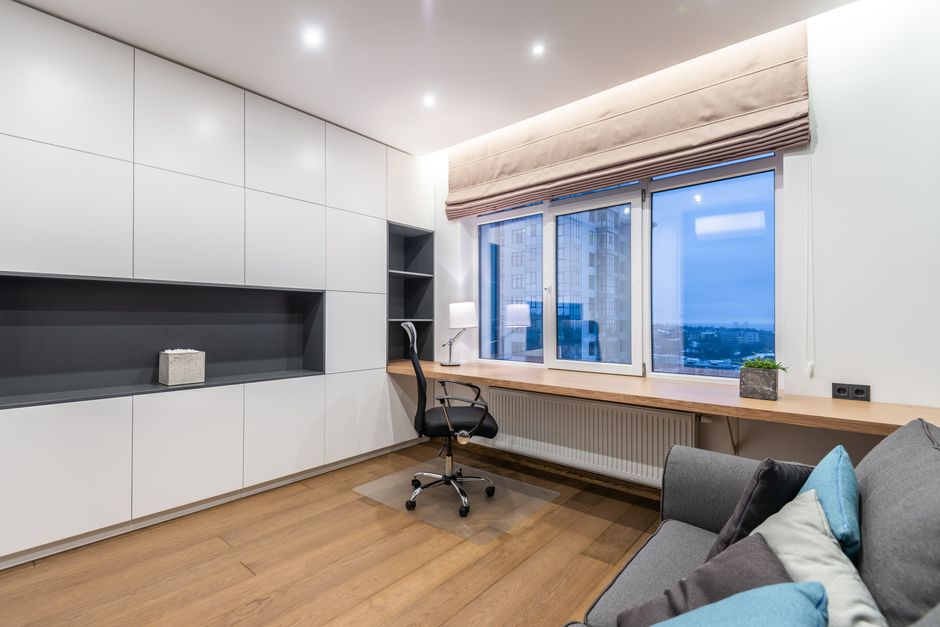 Armchair near wooden shelf between white cupboards and comfortable sofa with pillow in light stylish room with window at home