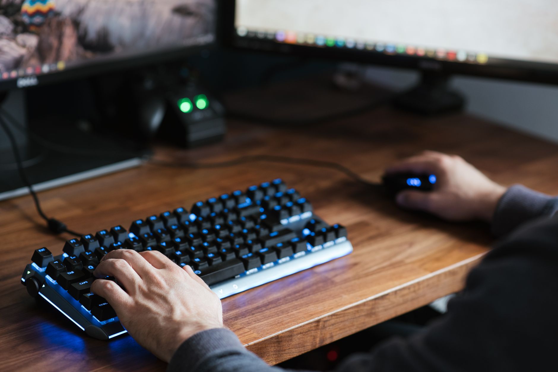 Person typing on a keyboard tucked under a wooden desk shelf in a home office