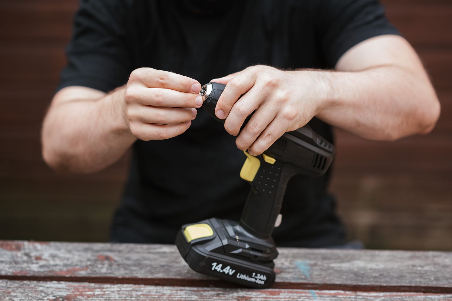 Hands using a cordless drill to bolt a steel desk frame leg to a wooden top