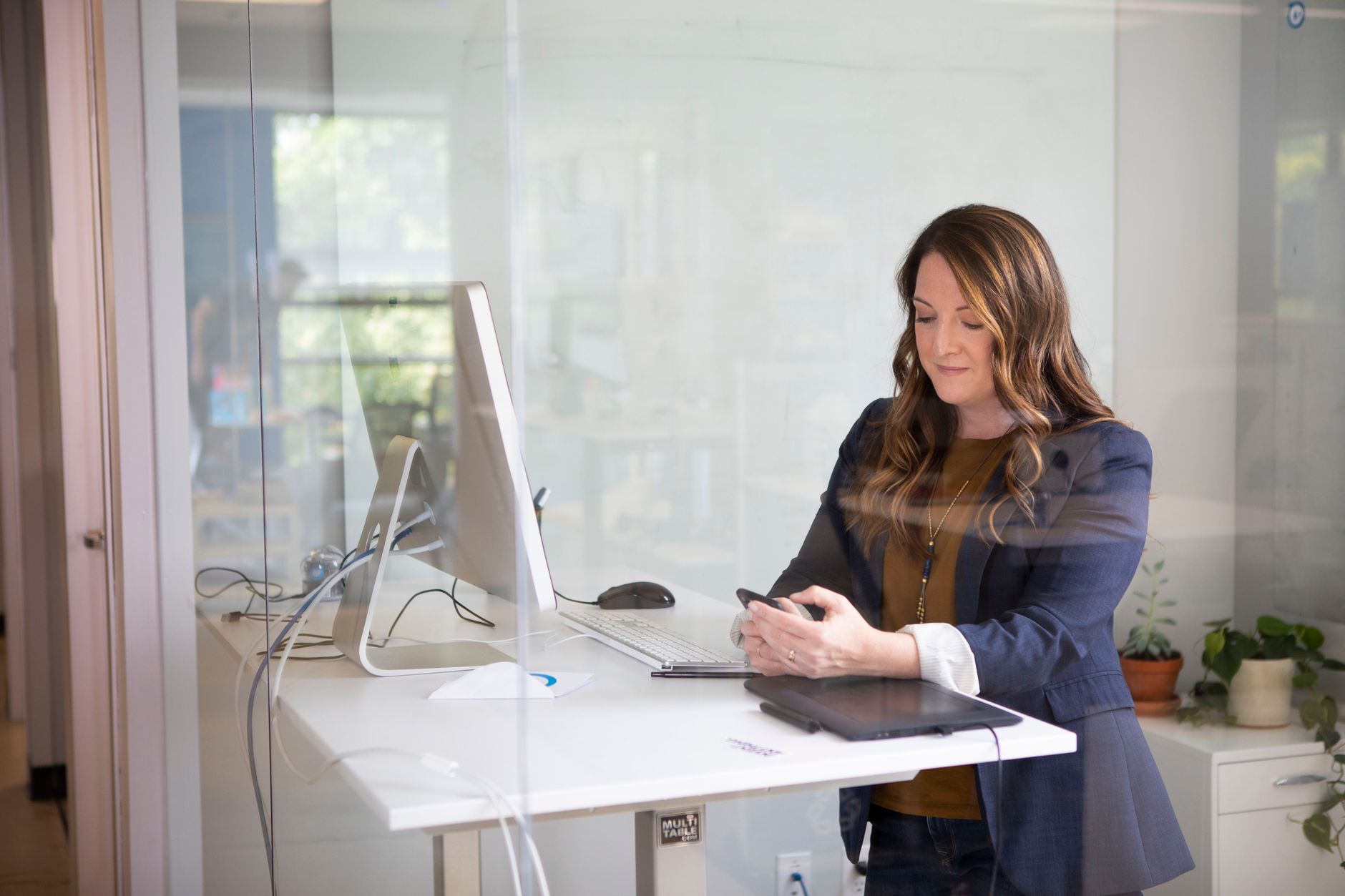 Person pressing a keypad to raise a standing desk with a wooden top in a bright office